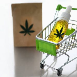Cart from the supermarket with bottle of hemp oil on gray background with reflection