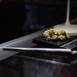 Close-up on raw marijuana placed on a weighing scale next to a rolled joint - focus on raw marijuana.